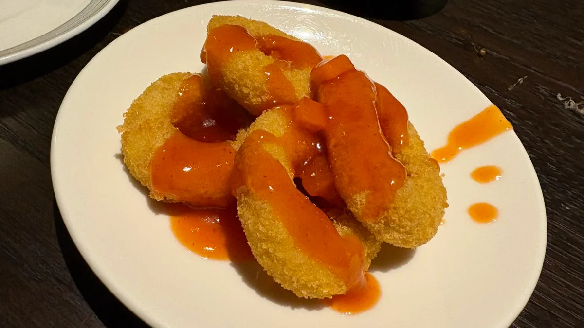 Ring-shaped pieces of breaded fried chicken coated in an orange-red sauce on a white plate