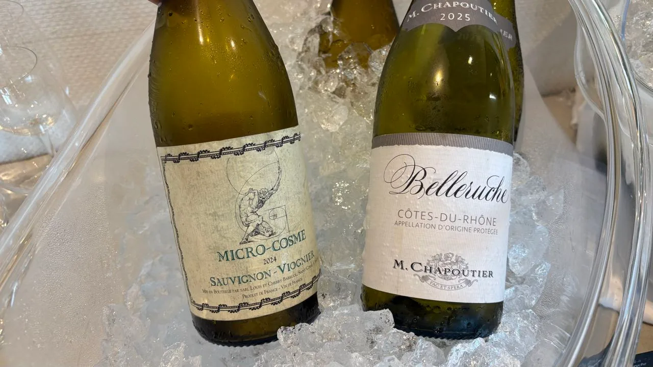 Two open white wine bottles lying in crushed ice, one labelled MICRO-COSME 2024 Sauvignon-Viognier and one Belleruche Côtes-du-Rhône by M. Chapoutier