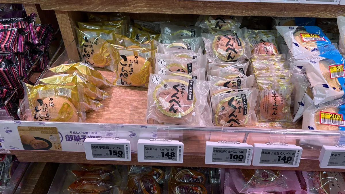 A supermarket shelf of round sweets in individual packets, gold konpen on the left and clear kunpen packets in the middle, with electronic price tags below