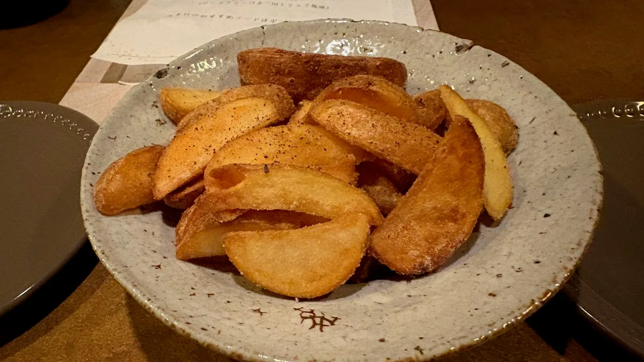 A ceramic bowl of thick fried potato wedges dusted with black pepper on a counter