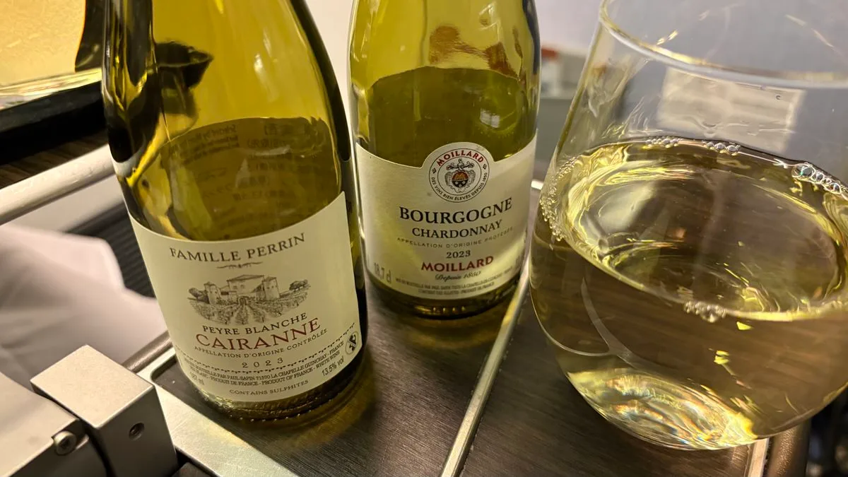 Two small bottles of white wine standing on an aircraft tray table beside a glass of white wine