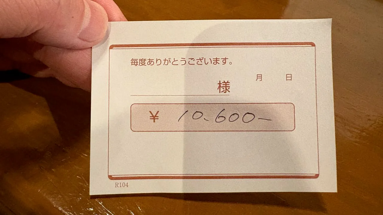 A small printed bill slip held between finger and thumb, with 10,600 written by hand in the box in the middle