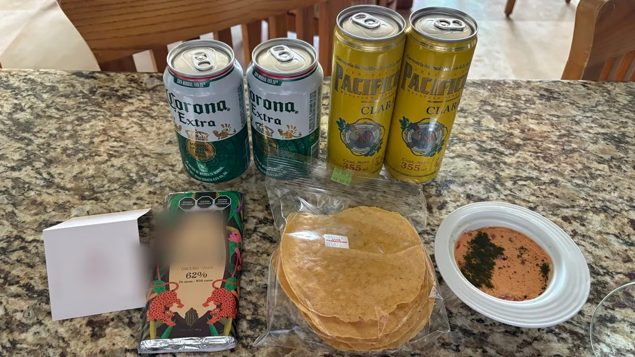 Two cans of Corona Extra and two of Pacifico Clara on a granite counter, with a 62% dark chocolate bar, a bag of tostadas and a bowl of dip